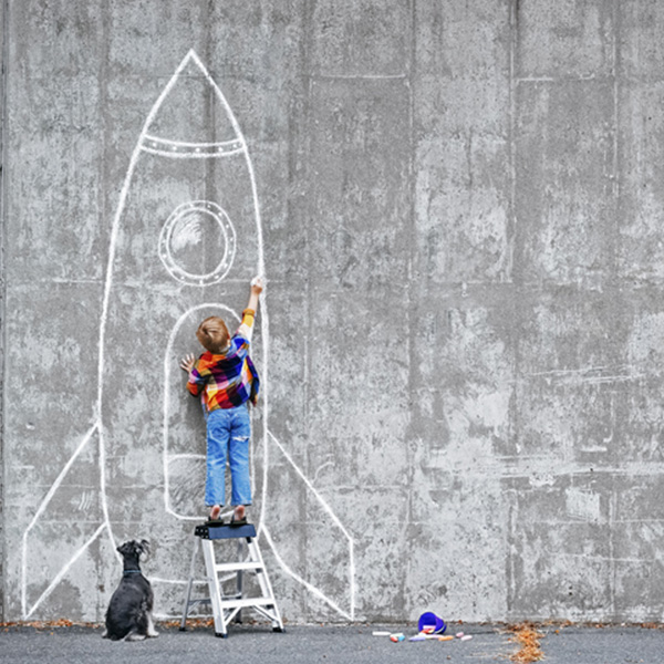 Enfant sur un escabot qui dessine une fusée